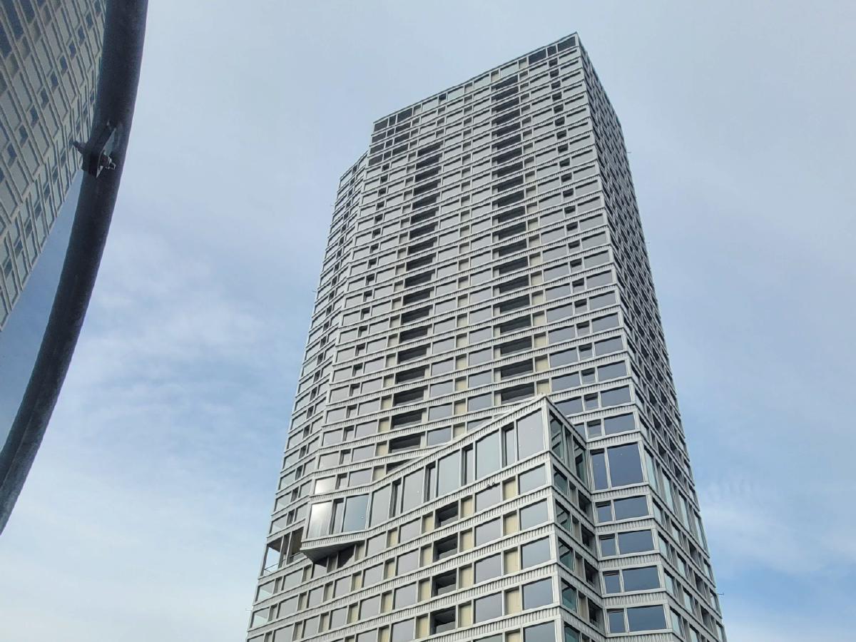 Modernes Hochhaus mit einzigartiger Architektur unter blauem Himmel, innovatives Design und urbanes Leben.