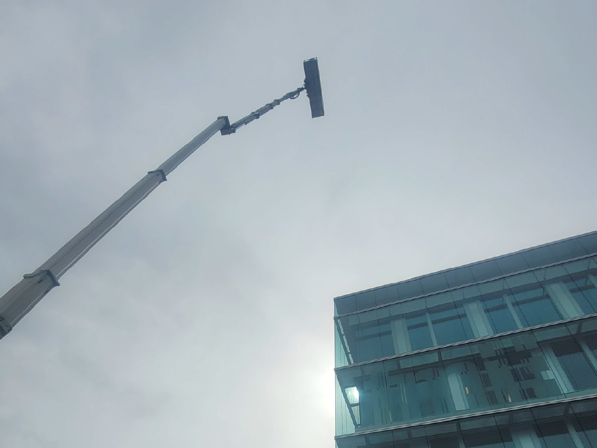 Kran mit Reinigungsvorrichtung reinigt die Glasfassade eines modernen Bürogebäudes bei bewölktem Himmel.