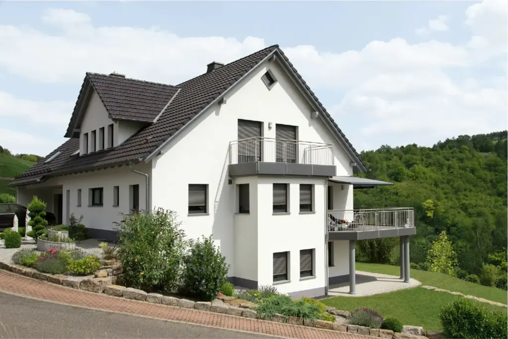 Modernes Einfamilienhaus mit gepflegtem Garten, grauem Dach und Balkonen in ruhiger, grüner Umgebung.