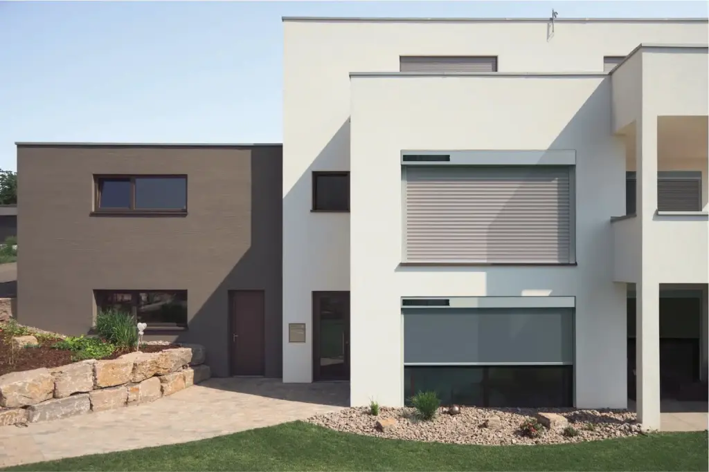Moderner zweifarbiger Hausbau mit großen Fenstern und gepflegtem Garten vor dem Eingangsbereich.
