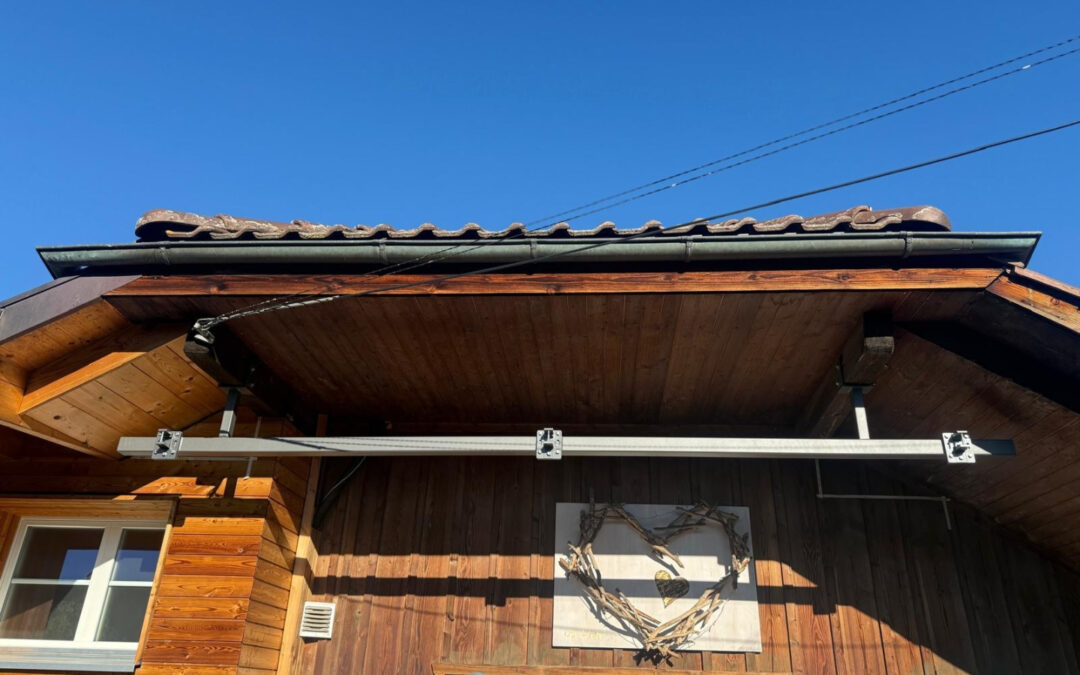 Holzchalethaus mit Herzdeko unter Dachvorsprung und blauem Himmel im Hintergrund.